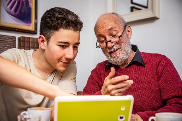 junger Mann im Gespräch mit älterer Frau, junge Frau und älterer Mann mit iPad