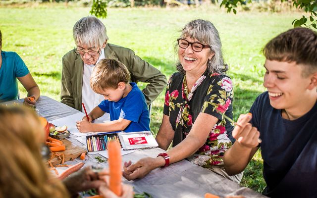 Menschen verschiedener Altersgruppen sitzen zusammen im Park an einem grossen Tisch