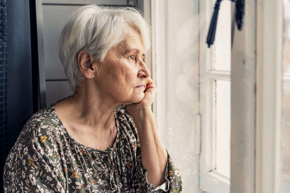 Eine einsame Seniorin schaut traurig aus dem Fenster.